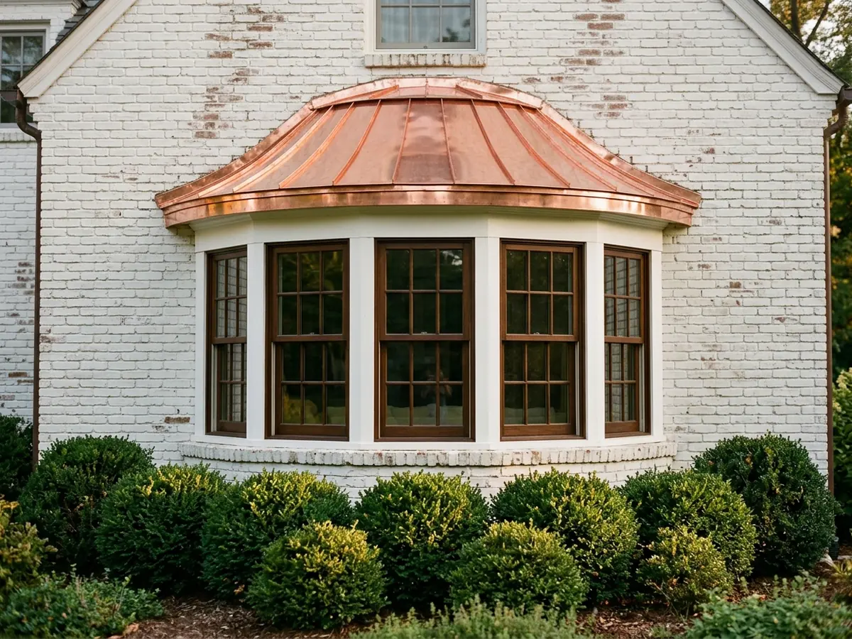 Curved bay window on a white-painted brick house with a small copper standing seam roof and copper drip edge, boxwoods below
